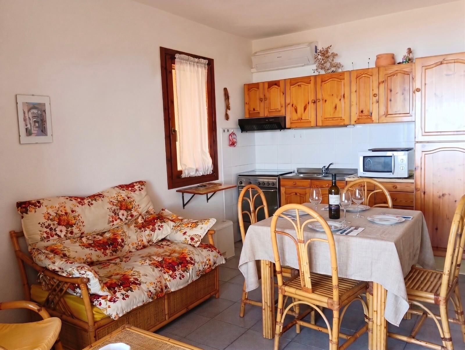 Un ambiente compatto con divano, tavolo da pranzo, sedie, angolo cottura dotato di elettrodomestici e una finestra con tende.