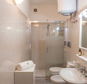 Et moderne badeværelse med en glasvæg omkring bruseren, et toilet, en håndvask og et håndklæde på en bordplade.