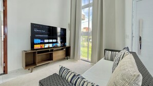 A living room with a flat-screen TV, a sofa, and a window with curtains. - Beach house in a beachfront condominium with 3 en-suite bedrooms, Wi-Fi. (Caucaia)
