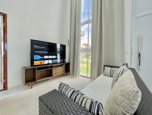 Ein Wohnzimmer mit Flachbildfernseher, einer Couch und einem fenster mit Vorhängen.