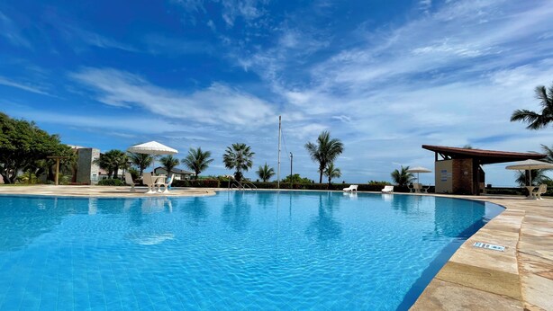 A swimming pool with lounge chairs, palm trees, and a clear sky. - Beach house in a beachfront condominium with 3 en-suite bedrooms, Wi-Fi. (Caucaia)