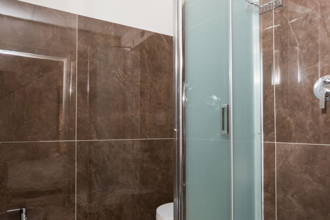 Een badkamer met een douchecabine van glas, een wit toilet en bruine marmeren tegels.