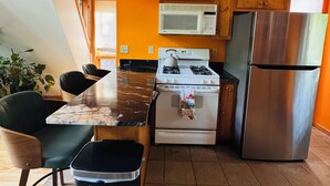 A kitchen with a gas stove, microwave, refrigerator, wooden cabinets, and a trash bin.