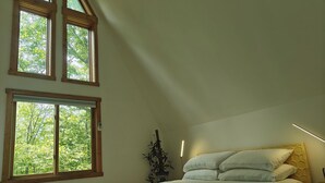 A bedroom with a bed, two windows, a wall-mounted light, and a plant.