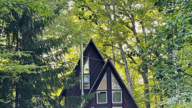 A cabin with a triangular roof, a balcony, and a gravel driveway.