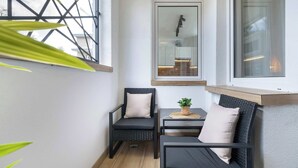 Habitación de esquina con dos sillas negras, una mesita, una planta en maceta y ventana con vistas a un edificio.