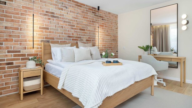 Un dormitorio moderno con pared de ladrillo, cama de madera, mesitas de noche, escritorio y espejo.