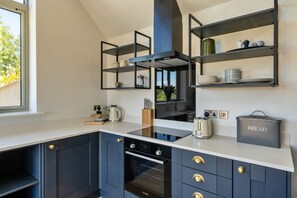 A modern kitchen with dark cabinetry, white countertops, and built-in shelves. - The Cart Shed (St Issey)