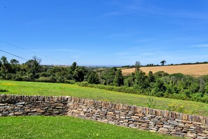 A stone wall, grassy field, and trees under a clear sky. - The Cart Shed (St Issey)