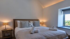 Uma cama bem arrumada com almofadas e toalhas, uma mesa de cabeceira com abajur e uma janela com vista.