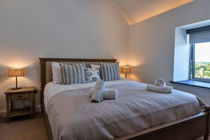Ein ordentlich bezogenes Bett mit Kissen und Handtüchern, ein Nachttisch mit Lampe und ein Fenster mit Blick.