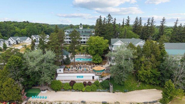 Un resort con una piscina grande, zona de playa y varios edificios rodeados de árboles.