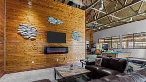 Una sala de estar acogedora con una pared de madera, un televisor de pantalla plana, una chimenea, una mesa de billar y un sofá de cuero.