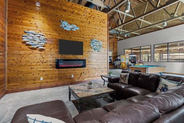 A cozy living room with a wooden wall, a flat-screen TV, a fireplace, a pool table, and a leather couch.