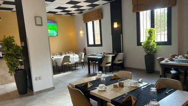 A restaurant with tables set for dining, a TV screen, and potted plants.