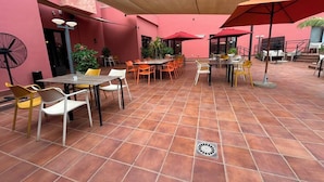 An outdoor patio area with tiled flooring, tables, chairs, and umbrellas providing shade.