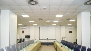 Una sala de conferencias con una larga mesa, sillas, una pantalla de proyector y una pizarra.