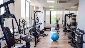 A gym with various exercise equipment, a blue exercise ball, and large windows.