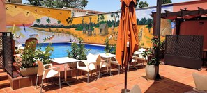 An outdoor patio with a swimming pool, white chairs, and a mural on the wall. - LE GRAND HOTEL DE THIES (Thies)