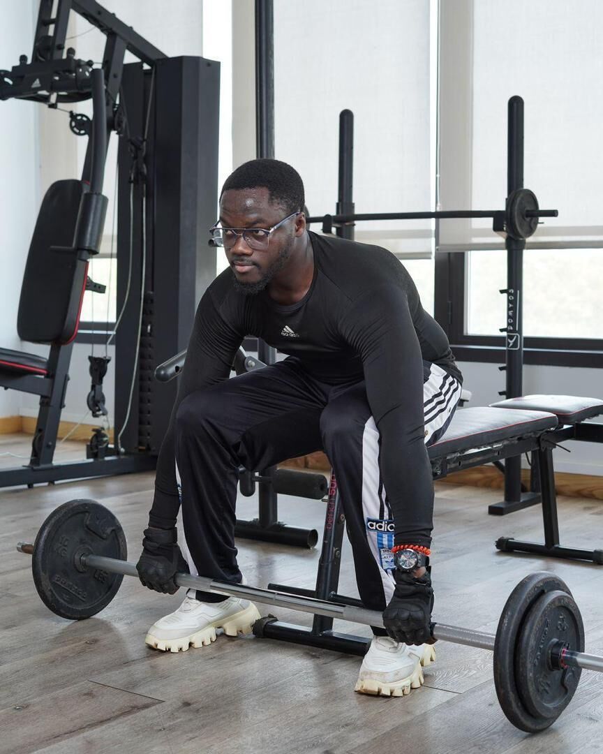 A person seated on a bench in a gym with weightlifting equipment.