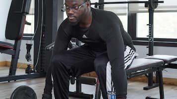 A person seated on a bench in a gym with weightlifting equipment.
