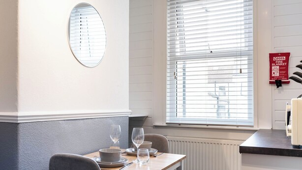 En spiseplads med et bord dækket til to, et vindue med persienner, et brandskilt og en radiator.