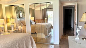 Une chambre à coucher comprenant un lit, des tables de chevet, un miroir et une vue sur une autre pièce grâce à une cloison en verre.