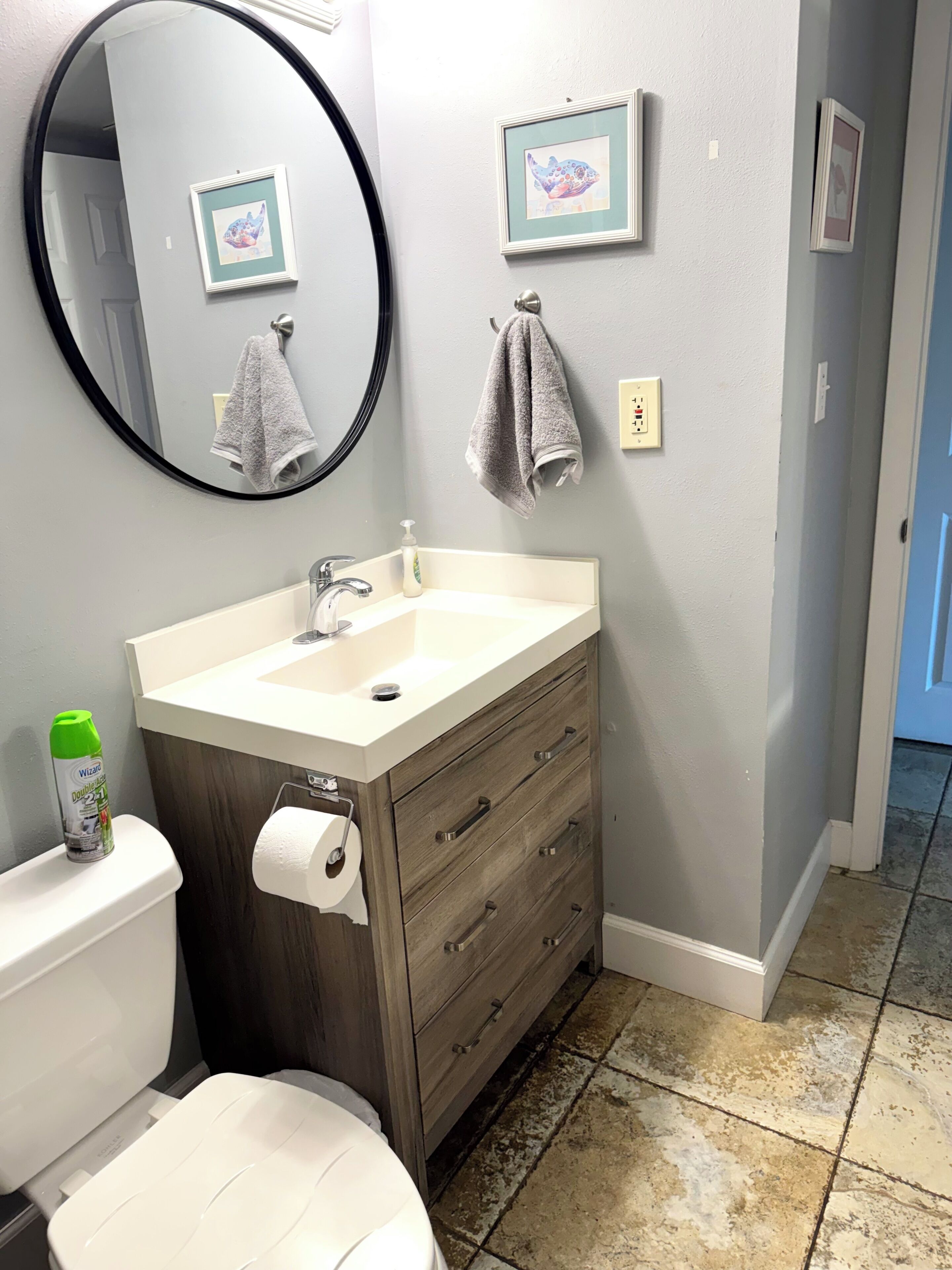 A bathroom with a toilet, sink, and mirror. There are two framed pictures on the wall.