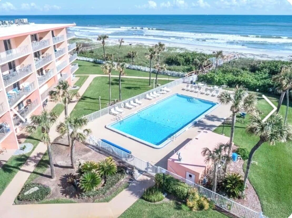 Een hotel met een zwembad, palmbomen en uitzicht op de oceaan.