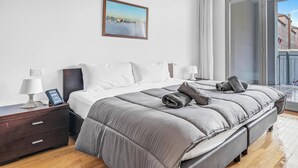 Une chambre moderne avec un grand lit, des tables de chevet, un tableau et une vue sur l’extérieur, visible à travers une porte coulissante.