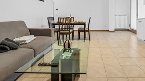 Un salon comprenant une table basse en verre, un canapé, une table à manger avec des chaises et un climatiseur fixé au mur.