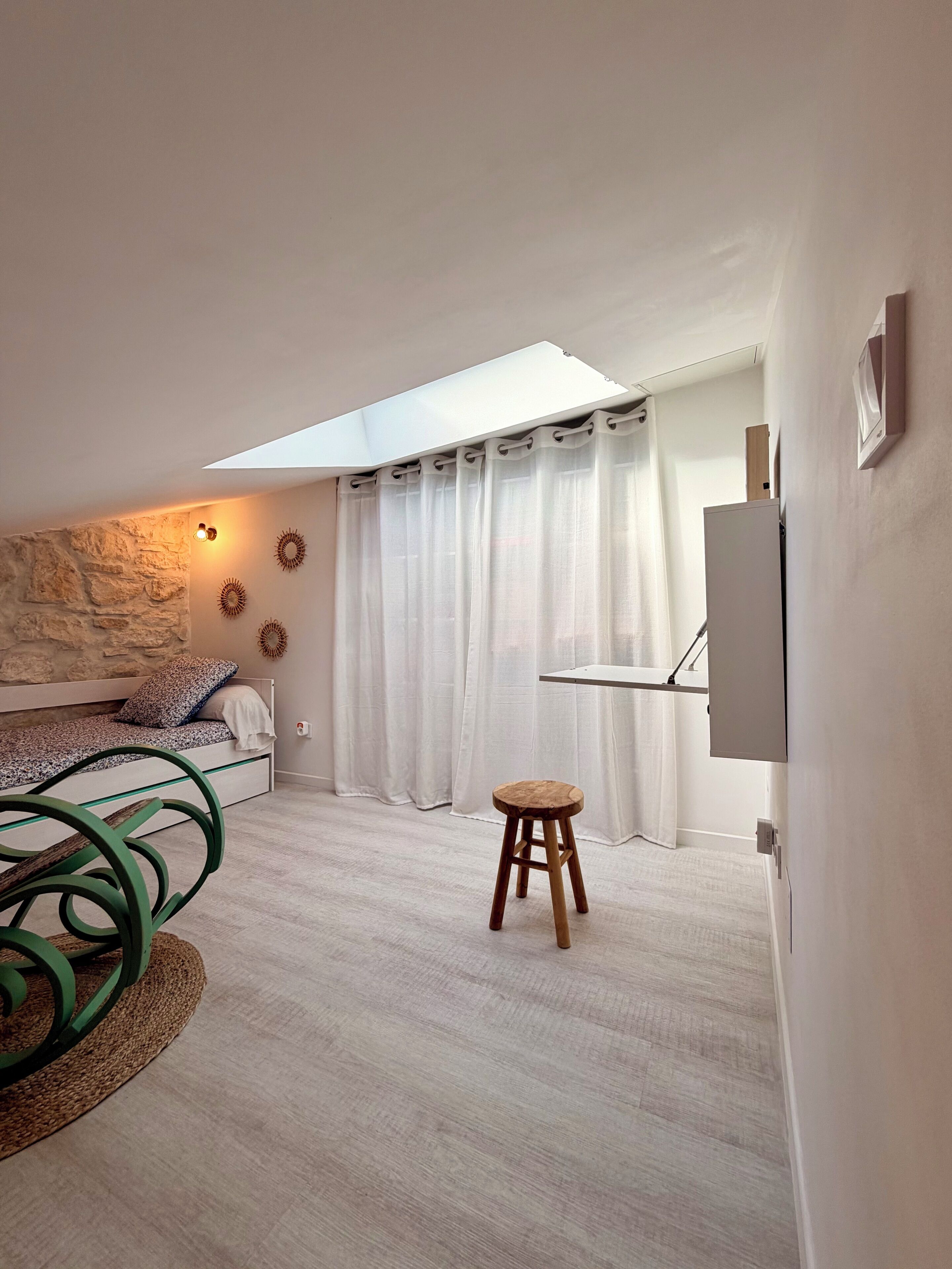 Ein modernes Schlafzimmer mit Oberlichter, einem Bett mit gemustertem Kopfteil, einem kleinen Hocker und einem am Wand montierten Fernseher.