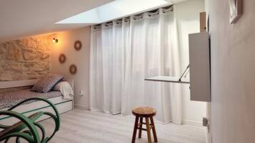 Ein modernes Schlafzimmer mit Oberlichter, einem Bett mit gemustertem Kopfteil, einem kleinen Hocker und einem am Wand montierten Fernseher.