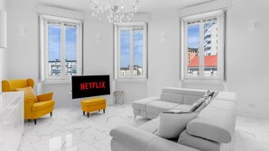 Ein modernes Wohnzimmer mit einem großen Flachbildfernseher, einem gelben Sessel, einem grauen Sofa und einer Kristallleuchtreihe.