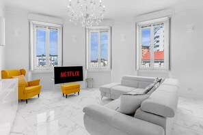 Ein modernes Wohnzimmer mit einem großen Flachbildfernseher, einem gelben Sessel, einem grauen Sofa und einer Kristallleuchtreihe.