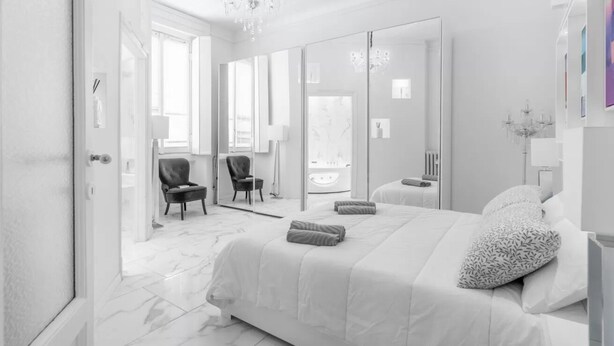 Ein modernes Schlafzimmer mit einem großen Bett, einem Spiegel, einer Kandelaber und Blick ins Badezimmer.