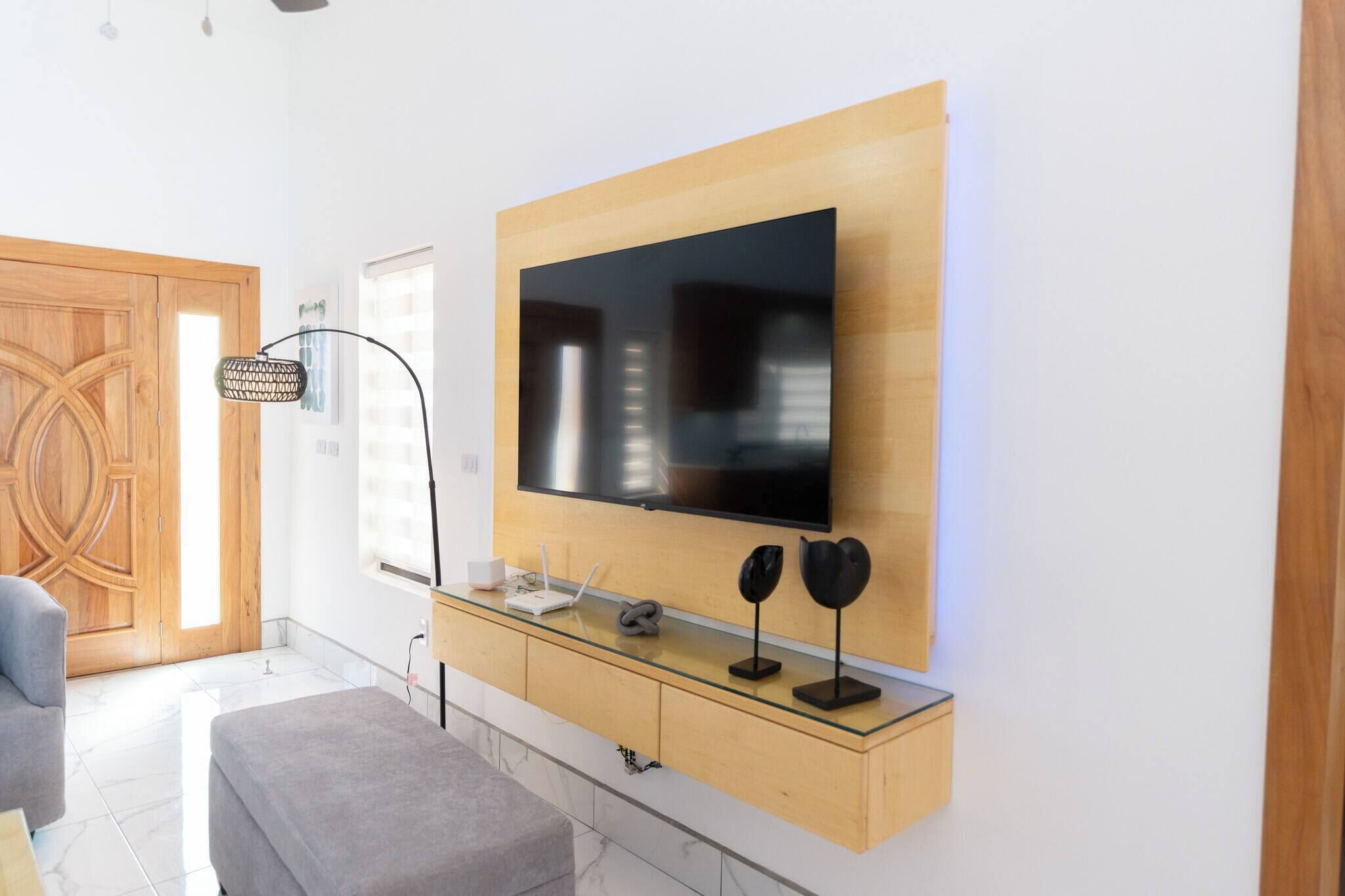 Ein modernes Wohnzimmer mit einem wandmontierten Fernseher, einem Glastisch und einer Holzkommode darunter.