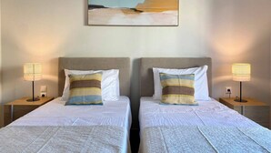 A hotel room with two beds, each with a headboard, bedside lamps, and a painting above. - Cosy apartment In the heart of Varkiza 100 meters from the Sea and all Shop area (Vari)