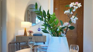 A dining area with a round table set for two, a potted plant, and a mirror above the table. - Cosy apartment In the heart of Varkiza 100 meters from the Sea and all Shop area (Vari)