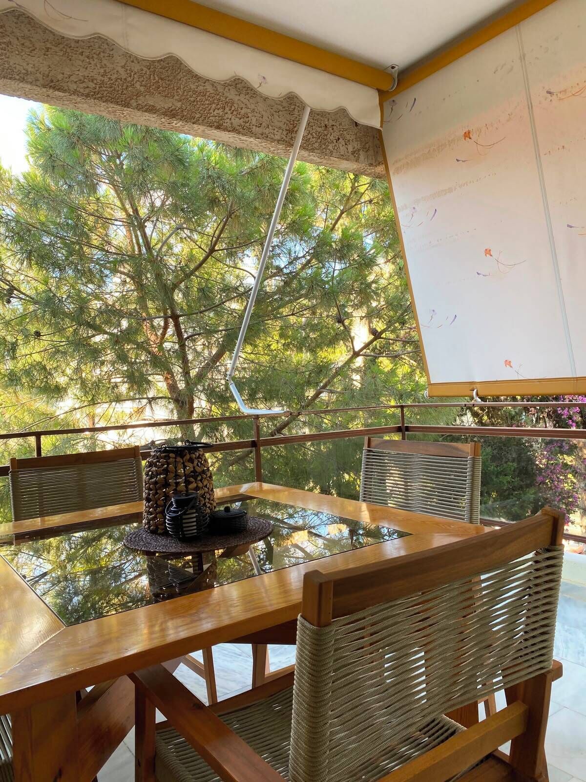 A wooden table with woven chairs, a whiteboard, and a view of trees through a window.