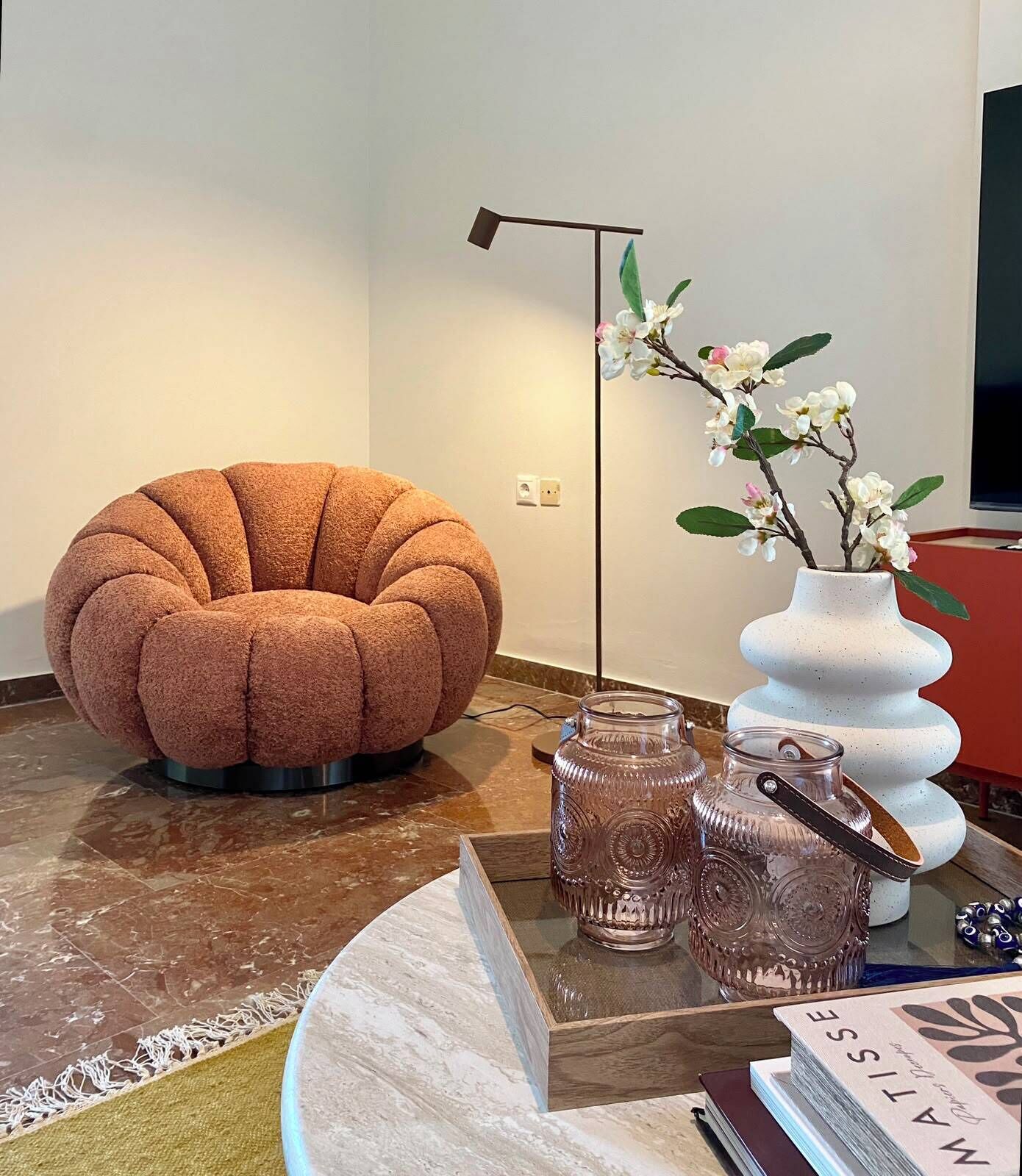 Ein modernes Wohnzimmer mit einem runden, strukturierten Sofa, einer Stehlampe, einer Vase mit Blumen und dekorativen Glasbehältern.