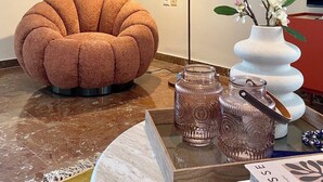 A modern living room with a round, textured sofa, a floor lamp, a vase with flowers, and decorative glass jars. - Cosy apartment In the heart of Varkiza 100 meters from the Sea and all Shop area (Vari)