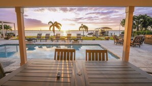 Ein Poolbereich mit Liegestühlen, einem Tisch und Blick auf den Sonnenuntergang über dem Meer.