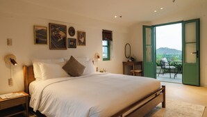 Un dormitorio con una cama grande, una mesita de noche, un espejo y vistas a un área exterior a través de una puerta abierta.
