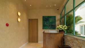 Zona de recepción con un mostrador de madera, un cuadro en la pared y un ventanal con plantas afuera.