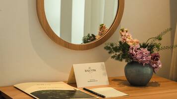 A wooden desk with a mirror, a vase with flowers, and a welcome card.