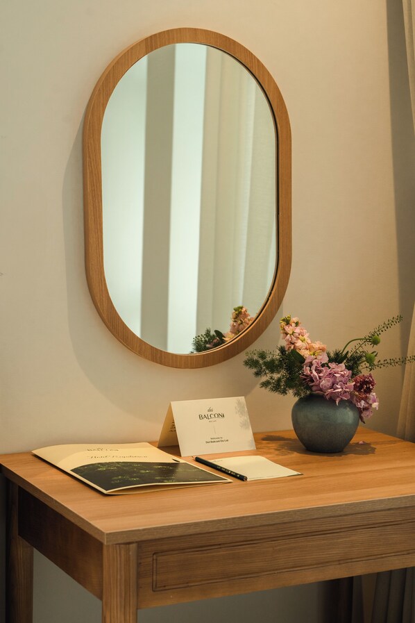 A wooden desk with a mirror, a vase with flowers, and a welcome card. - Dei Balconi Dalat (Xuan Huong - Da Lat)