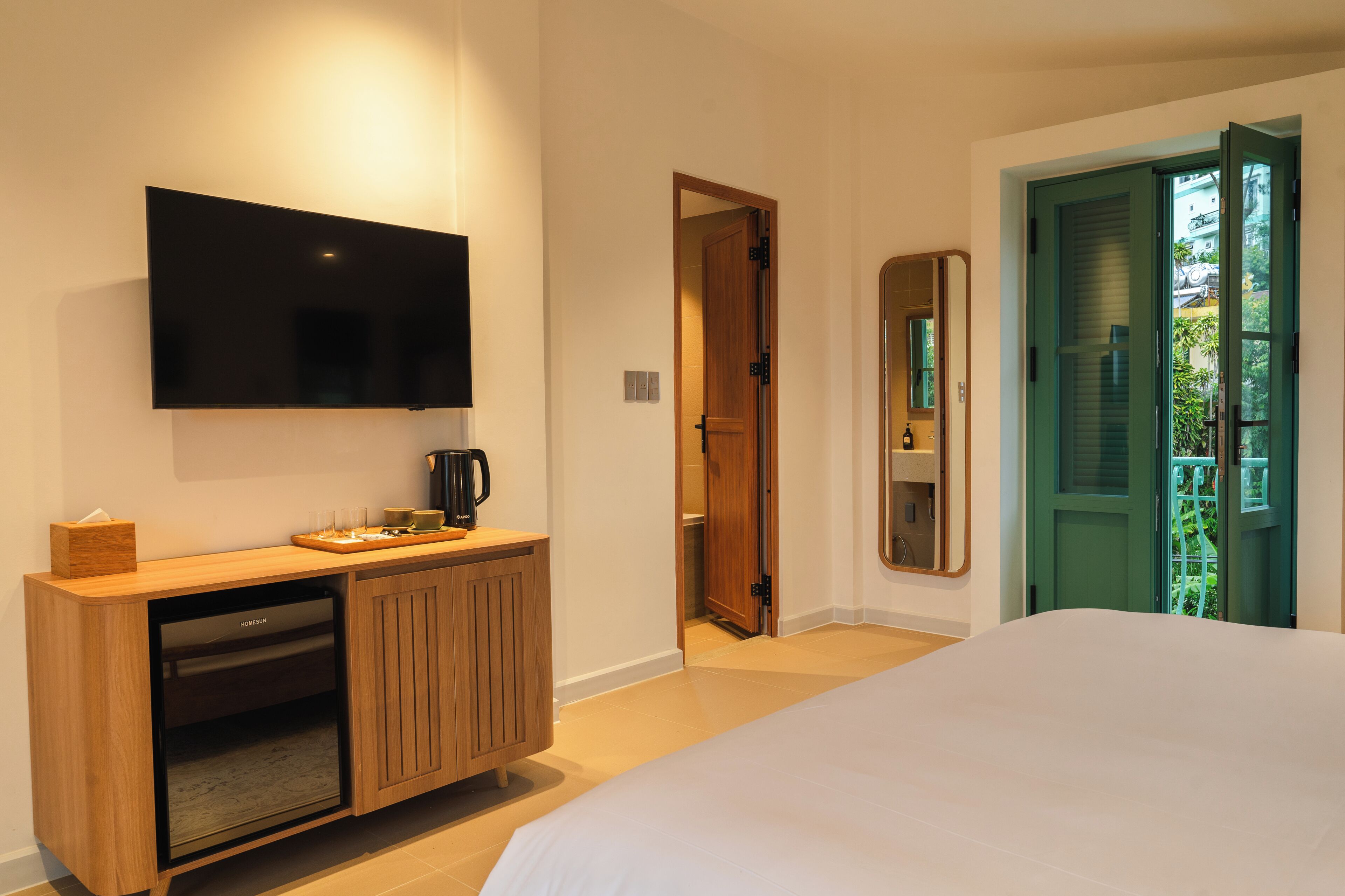 A hotel room with a bed, a TV mounted on the wall, a wooden cabinet, and a door leading to a balcony.