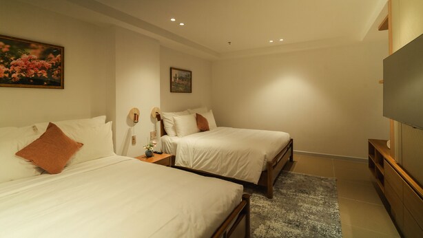 Una habitación de hotel con dos camas, un televisor de pantalla plana, un cuadro y una mesita con un florero.