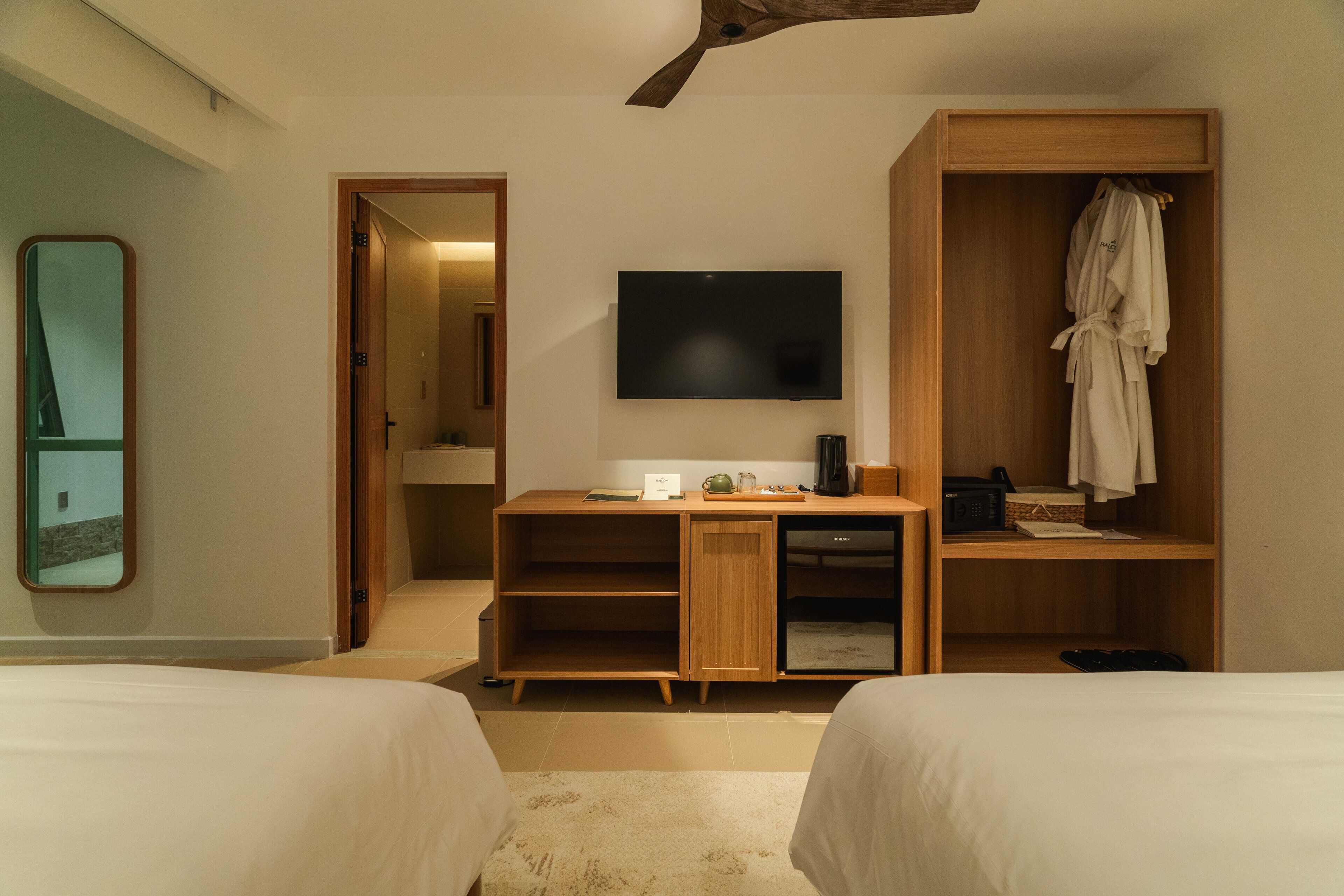 A hotel room with two beds, a desk with a flat-screen TV, a wardrobe, and a mirror.